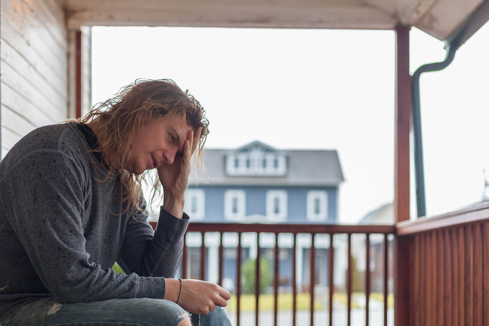 man with long hair sitting on porch displeased